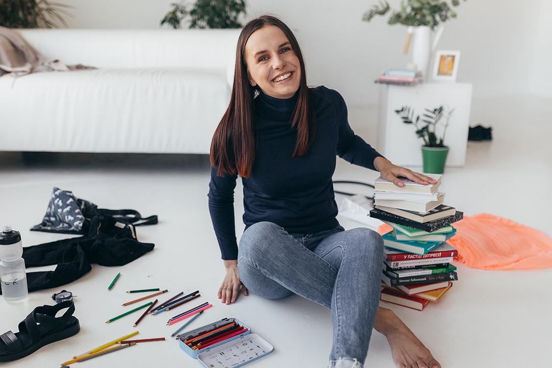 The smiling girl is sitting next to a pile of books